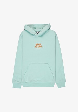 Sudadera con capucha verde claro con bolsillo frontal y texto de logo marrón, combinada con vaqueros azules holgados y zapatos negros. Estilo informal de ropa urbana.