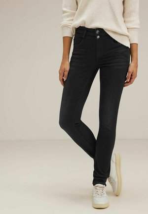 Jeans skinny neri con una texture liscia, caratterizzati da una vita standard, due tasche frontali e due tasche posteriori, abbinati a un maglione bianco semplice.