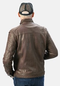 Bruine leren jas met een staande kraag, gestepelde schouderaccenten en kenmerkende stiksels. Draag het met een blauwe spijkerbroek en een zwarte mesh pet.