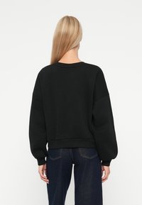 Sudadera negra de corte relajado, con puños y dobladillo acanalados. Textura suave con hombros caídos y escote redondo, combinada con jeans azul oscuro.