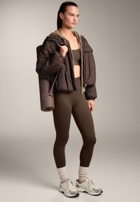 Barna puff dzseki bézs béléssel, barna crop top és passzos Leggings. Görgő jogamat visz, fehér és szürke sportcipőben.