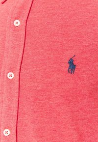 Polo shirt corto rosso a maniche corte in cotone testurizzato, con una patta a due bottoni e logo ricamato blu scuro sul lato sinistro del petto.