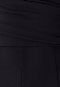 Čierna tkanina s hladkou textúrou, s drapériou a preloženými akcentmi v hornej časti, ktoré prechádzajú do priliehavého úseku nižšie.