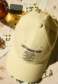 Gelbe Baseballmütze aus Baumwolle mit schwarzer gestickter Schrift, die Städtenamen auflistet. Rundes Schild und deutlich sichtbares Knopfdetail oben.