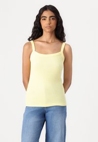 Yellow ribbed tank top with wide straps and a square neckline, paired with light blue denim jeans. Smooth texture, form-fitting design.