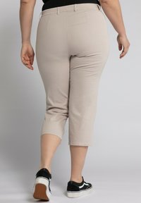 Pantalons capri beige clair avec une texture lisse, taille élastique et poches arrière. Associés à des baskets noires avec une accentuation blanche.