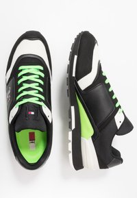 Černo-bílé sportovní boty s zelenými akcenty, sesterou sítí, plochými tkaničkami a texturovanou podešví pro lepší přilnavost.