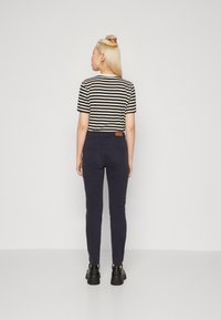 Csíkos fekete és fehér rövid ujjú felső, sötét tengerészkék, slim-fit farmernadrággal párosítva; hátul bőr címke található a derekán, és fekete cipő övezi.