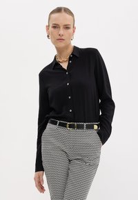 Camicia nera con colletto. Abbinata a pantaloni a vita alta con motivo monocolore e una cintura nera con fibbia dorata.