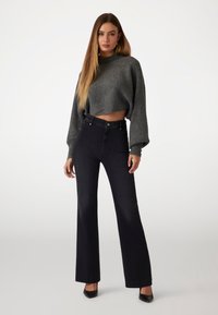 Gray cropped sweater with a textured finish paired with high-waisted black flared jeans featuring side button accents. Black heels complete the look.