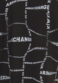 Černá tkanina s rozptýleným bílým textem, na kterém je napsáno "ARMANI EXCHANGE" a "AIX" v různých velikostech a orientacích, vytvářející dynamický vzor.