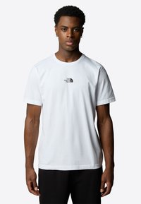 Hvid bomuld t-shirt med korte ærmer, der har et lille sort logo på brystet. Enkel, klassisk design med rund hals.