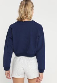 Námorně modrá zkrácená mikina s dlouhými rukávy, žebrovanými manžetami a kulatým výstřihem; kombinována se světle šedými tečkovanými šortkami.