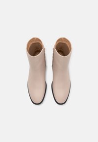 Béžové kotníkové boty s hladkým povrchem, kulatou špičkou a černou podrážkou. Mají zip na boku pro snadné obouvání.
