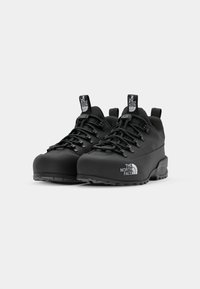 Black hiking shoes with a textured finish, featuring rounded toes, sturdy laces, and a prominent logo on the side and heel.