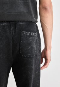 Svart denim joggesko med teksturert finish, med en lomme på høyre side og elastisk liv for komfort.