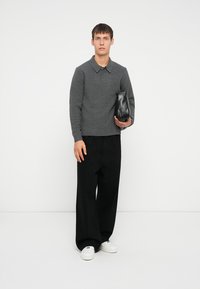 Suéter gris de punto con un cuello tipo camisa, combinado con pantalones anchos negros y zapatillas blancas, sosteniendo un bolso de cuero negro.