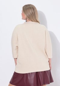 Beżowa, oversize bluzka z rękawami 3/4, z czystym szwem z tyłu; zestawiona z bordową spódnicą z sztucznej skóry. Gładka faktura całości.