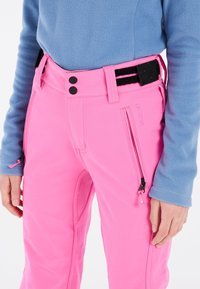Heldere roze skibroeken met een gladde textuur, twee zwarte knopen, zijzakken met rits en een zwart-wit gestreepte riem. bovenkleding