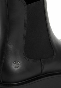 Black leather ankle boot with elastic side panels, featuring a rounded toe and a thick sole. Logo embossed on the outer side.