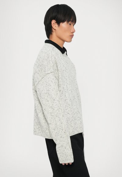 Lys grå strikkegenser med en teksturert finish, oversized passform og svart krage. Lange ermer med drop shoulder-design og sideslisser i kanten.