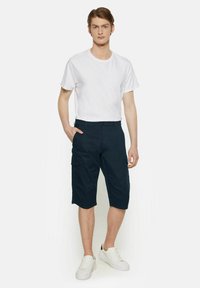 Pantaloni scurți cargo navy din bumbac, cu buzunare laterale și închidere cu nasture, asortați cu un tricou alb simplu și adidași albi.