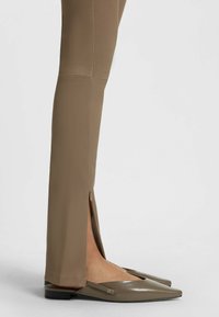 Fitted brown trousers featuring a side slit, paired with flat, pointed-toe shoes in a matching brown tone. Smooth texture throughout.