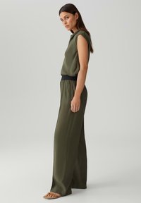 Olijfgroen cropped top gecombineerd met losse, hoge taille broek met een zwarte tailleband. Soepele textuur en vloeiende stof.
