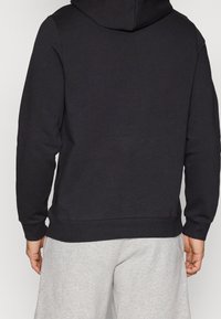 Sweat à capuche noir avec poche kangourou, capuche à cordon de serrage réglable et poignets côtelés. Le matériau semble doux et léger.