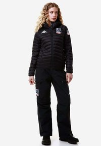 Giacca trapuntata nera con design a righe orizzontali, dotata di cappuccio integrato e logo degli Stati Uniti. Abbinata a pantaloni neri, anch'essi con loghi e cerniere.