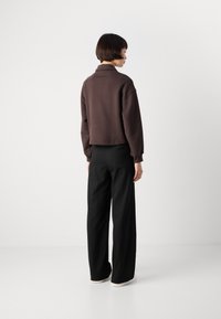 Brown cropped sweatshirt with a high collar, paired with black wide-leg trousers. Smooth texture, simple design, and minimalist style.