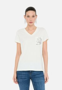 Camiseta blanca de cuello en V, hecha de tela suave, que presenta un bolsillo en el pecho con un diseño gráfico y el nombre de la marca "LIU-JO". Corte casual con mangas cortas.