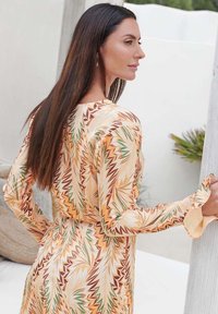 Langärmliges Kleid im gelb-creamfarbenen abstrakten Muster mit grünen Akzenten. Leichter Stoff mit einer taillierten Taille und ausladenden Ärmeln.