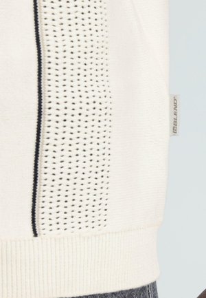 Λευκό πλεκτό ύφασμα με κάθετη ρίγα από μαύρες τελείες και ριμπ στο κάτω μέρος, με ετικέτα της μάρκας «BLEND» στη δεξιά πλευρά.