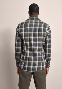 Kariertes Hemd in Grün, Blau und Weiß, mit langen Ärmeln und abgerundetem Saum. Der Stoff wirkt weich und hat ein Karomuster.
