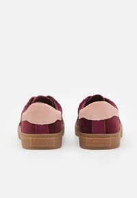Paire de baskets en daim bordeaux avec des accents rose clair au talon et des semelles en caoutchouc marron, vues de dos avec des étiquettes de talon portant la marque "GANT".
