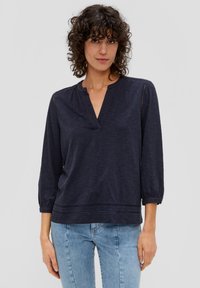 Dunkelblaues Oberteil mit Henley-Ausschnitt, dreiviertel Ärmeln und subtilen horizontalen Ausschnitten am Saum und an den Schultern. Weiche Textur.