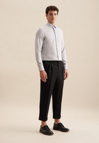 Camicia grigia con bottoni e motivo floreale sottile, abbinata a pantaloni neri a 3/4. Il modello indossa scarpe nere stringate. Sfondo semplice.