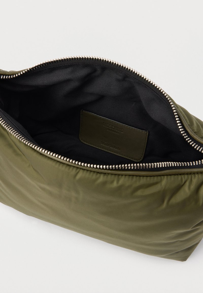 Olive green nylon pouch with silver zipper open to show black fabric interior and stitched rectangular label inside.