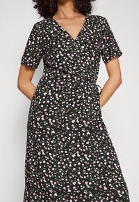 Zwarte jurk met korte mouwen, V-halslijn en wikkelontwerp. Bevat een bloemenpatroon in roze en wit met groene accenten.