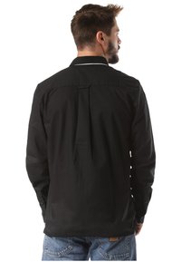 Camisa negra de manga larga con pliegue en la parte trasera, puños con botones y cuello plano. El material es suave, con textura mínima y un diseño limpio.