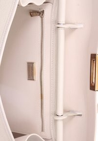Interno di una borsa in pelle bianca con una tasca con zip, accessori metallici, cuciture in pelle e un'etichetta che indica pelle autentica.