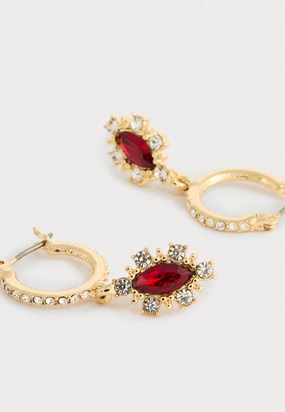 Auksiniai auskarai-žiedai su raudonu marquiso akmeniu, apsuptu mažų skaidrių kristalų ant paprasto šviesaus fono.