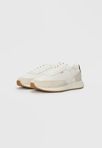 Hvite sneakers med overdel av semsket skinn og tekstil, gummisåle og snørebånd. Har subtil merkevare og en kontrasterende svart hæltab.