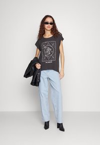 Grå grafisk t-skjorte med månedesign; kombinert med lyseblå vide jeans og svarte ankelstøvler. Svarte skinnjakke drapert over armen.