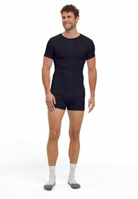 Czarna koszulka sportowa z krótkim rękawem i teksturowanym wzorem, w połączeniu z pasującymi czarnymi szortami, noszona przez męskiego modela.