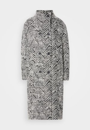 Manteau noir et blanc à motif en chevron avec un col haut, à double boutonnage à l'avant et deux grands boutons noirs. Design structuré.