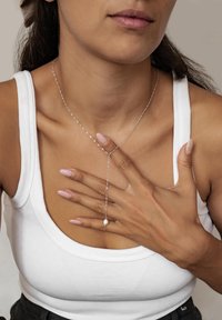 Collar de lariat de plata con un colgante de perla única, combinado con una camiseta sin mangas blanca con rayas. Las manos del modelo reposan sobre el pecho.