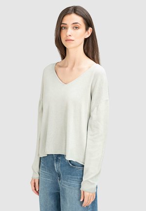 Pull gris clair à manches longues, col en V, avec une coupe décontractée et un ourlet légèrement court, fabriqué en tissu doux, porté sur un jean bleu.