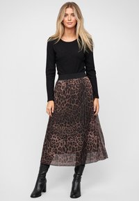 Zwarte geribbelde longsleeve-top gecombineerd met een doorschijnende maxi-rok met luipaardprint in bruine en zwarte tinten, aangevuld met zwarte laarzen tot de knie.